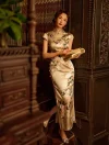 Sophisticated lady in a formal cheongsam featuring beautiful floral motifs, holding an old book and standing beside an antique dark wood cabinet.