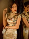 Lady wearing a formal cheongsam with short sleeves and red tassel earrings, looking into a mirror while holding a pearl beaded clutch bag.