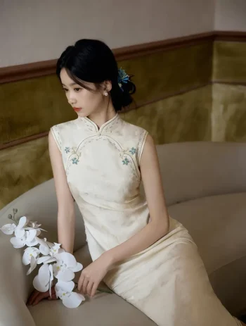 Graceful white qipao prom dress look featuring delicate blue floral embroidery and a model posing with a white orchid.