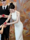 Close-up of a graceful woman in a beautiful halter cheongsam with a flattering fit, gently holding a red traditional teacup to serve guests during her engagement celebration.