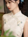 Close-up of the intricate blue flower embroidery and beaded button details on a high-collar white qipao dress.