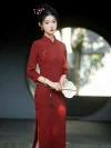 Elegant bride in a red long sleeve bridal qipao with intricate floral jacquard, holding a round white fan in front of a traditional Chinese moon gate.