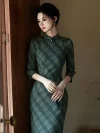 Sophisticated lady in a long sleeve cheongsam dress with classic green plaid and a pearl button collar, leaning gracefully against a wooden door frame in soft side lighting.