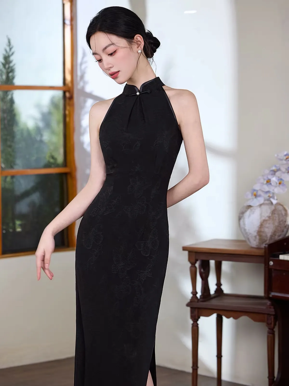modern-black-halter-cheongsam-side-slit Graceful look of a woman in a modern black halter cheongsam with subtle floral textures, looking down with her hair styled in a classic bun.