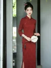 Beautiful woman standing gracefully in a refined qipao dress long sleeve with red embossed patterns, holding a tassel fan in a serene Chinese garden courtyard.