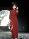 Stunning wedding portrait of a bride in a bright red bridal qipao featuring long sleeves, holding a pearl beaded bag while standing under dappled sunlight near a stone archway.