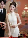 Elegant bride wearing a white halter cheongsam with delicate pearl decorations and a traditional floral headpiece, standing gracefully next to a groom in a black vest during a Chinese wedding.